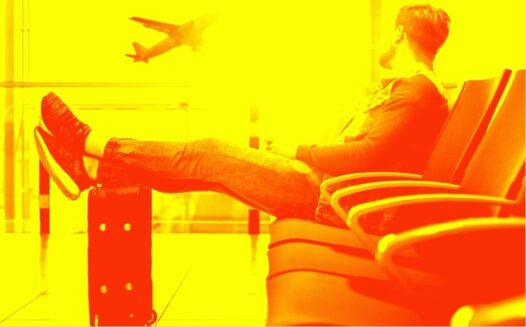 A man sits cross-legged at an airport and watches a plane take off.