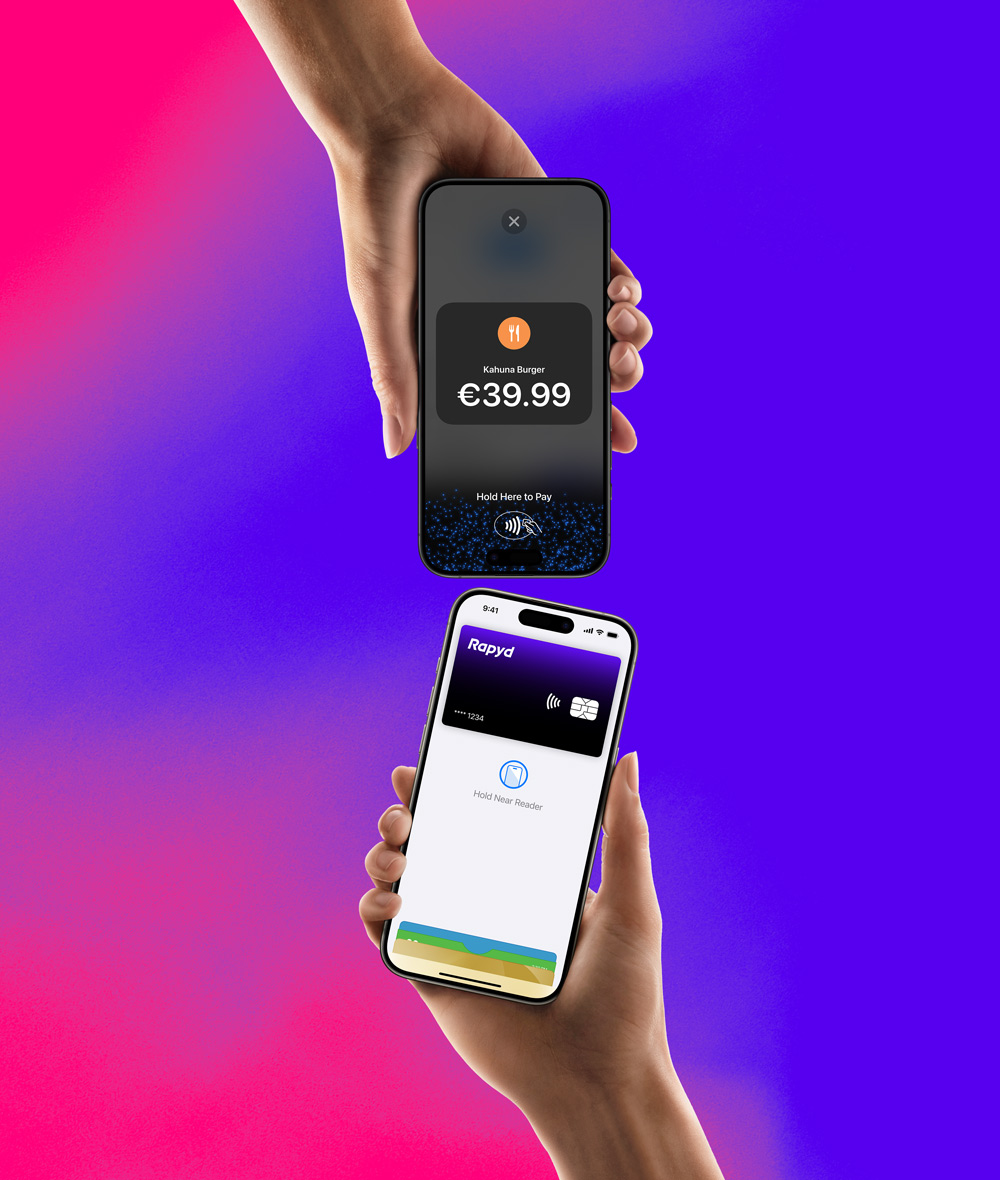 A hand holding an iPhone with a Rapyd credit card is about to pay on an iPhone that has a hold here to pay screen on it.